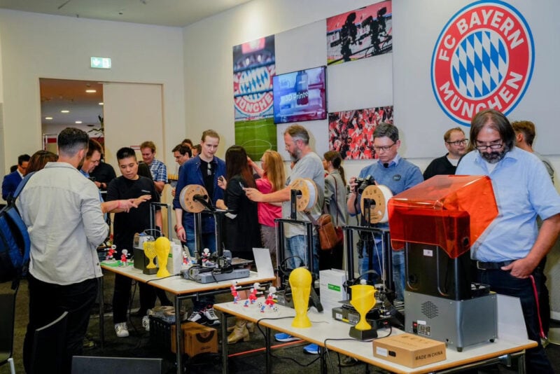 A group of people inspecting FDM and resin 3D printers at a launch event at the FC Bayern Munchen Stadium