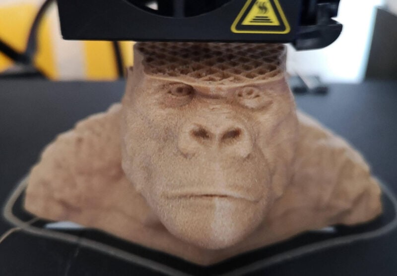 A 3D printer using wood PLA filament to create a gorilla bust.