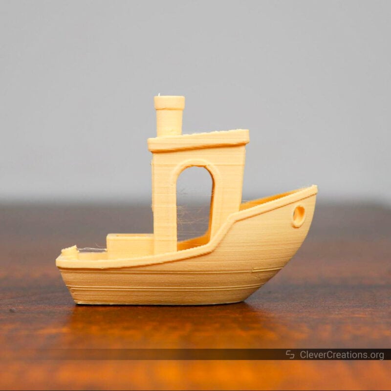 Close-up of a yellow 3D benchy model on placed on a table.