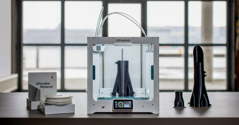 An Ultimaker 3D printer with various PC filament prints placed in and around it.