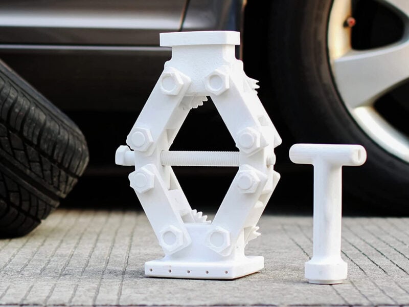A white 3D printed car jack in front of a car