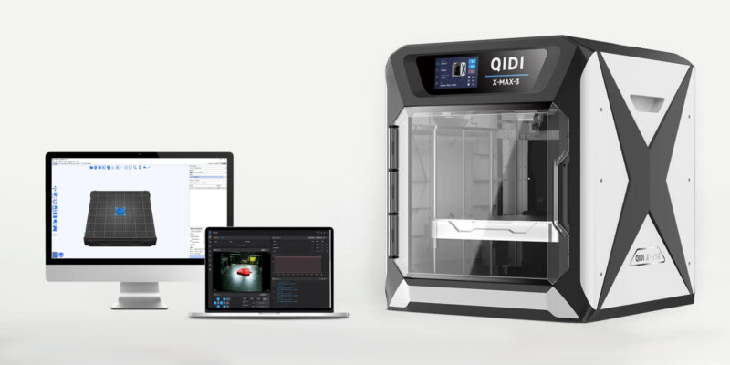 The QIDI X-Max 3 3D printer next to a computer screen and laptop.