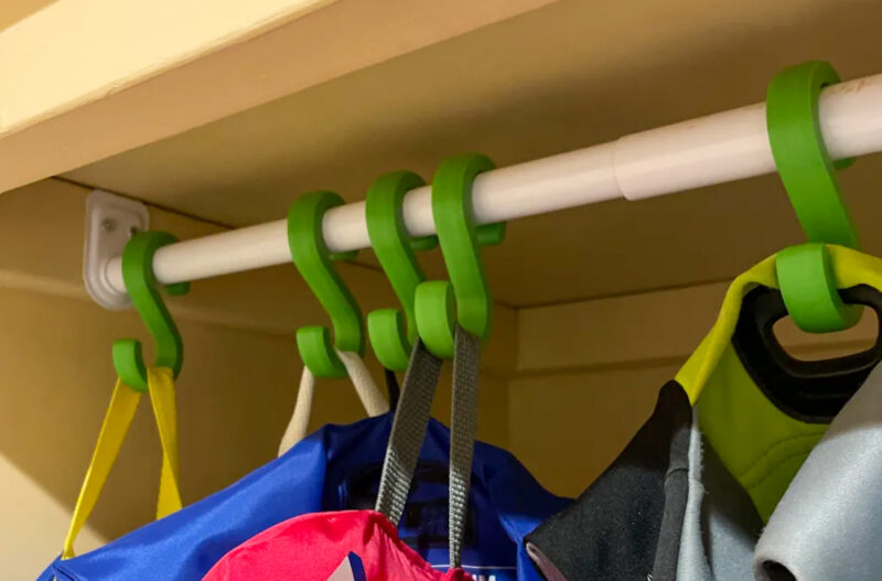Several green S-hooks 3D printed in ASA and used in a closet for hanging clothes.