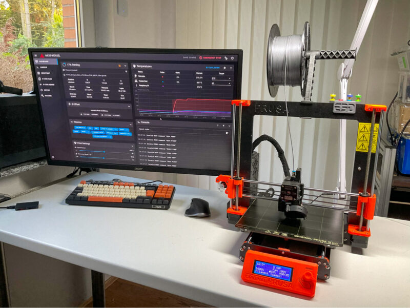 A DIY Klipper setup with a Prusa MK3S-i3 and web interface visible on a monitor.