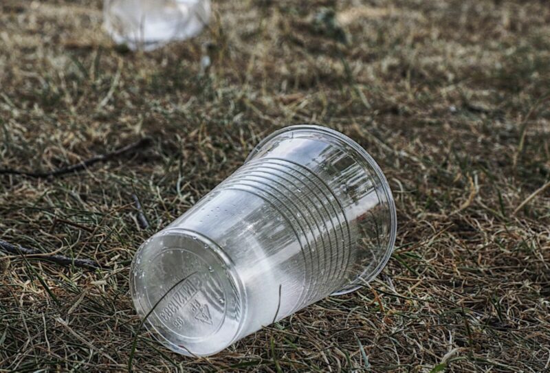A non-biodegradable plastic cup on a grass field.