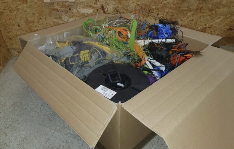A pile of ABS filament scraps and failed 3D prints collected in a box for recycling.