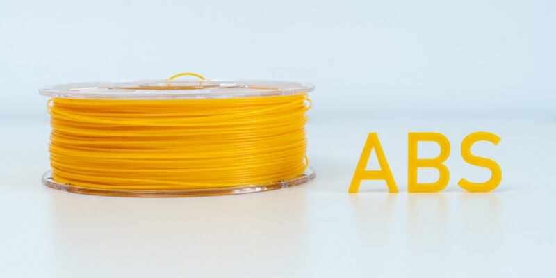 A roll of ABS 3D printing filament next to letters printed out of the same material.