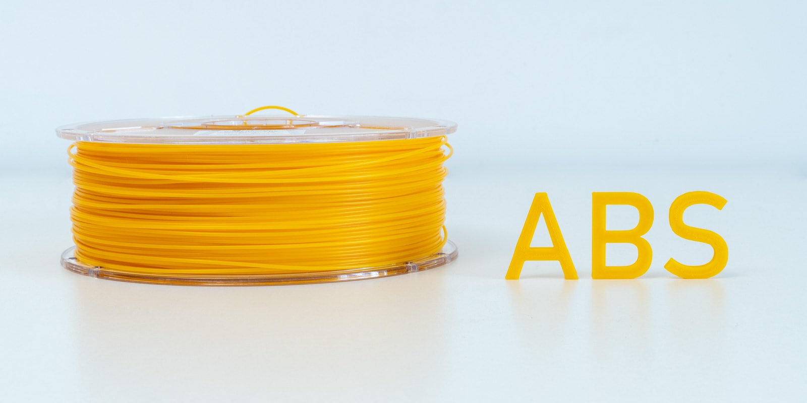 A roll of ABS 3D printing filament next to letters printed out of the same material.