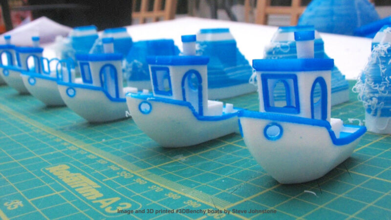 Several blue and white 3D printed multicolor Benchy 3D models used for configuring a dual extruder 3D printer.