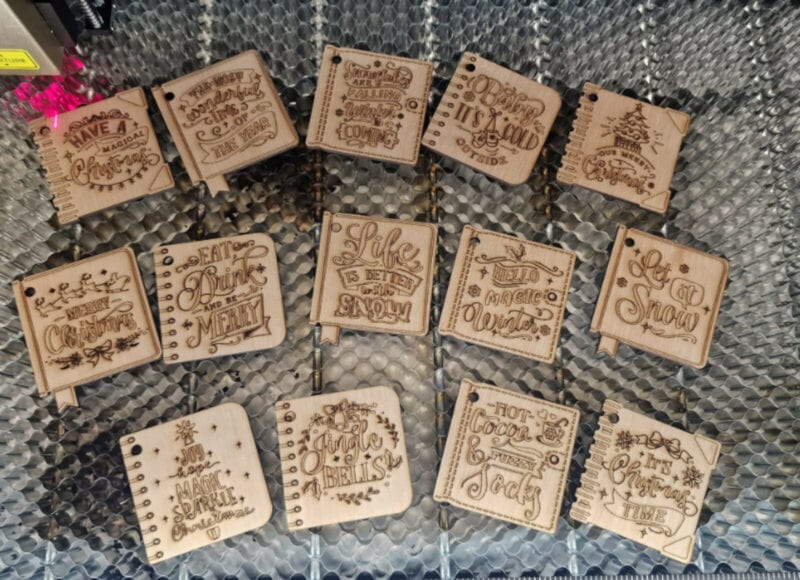 Many wooden engraved square book covers on a laser bed.