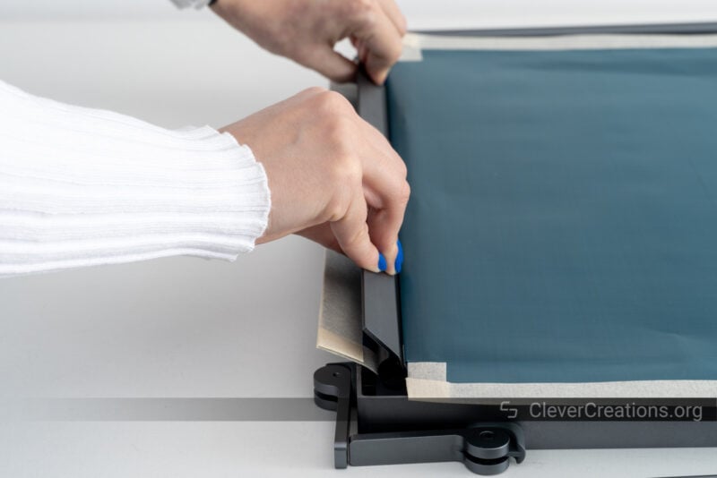 Two hands inserting a fixing bar into a frame to secure a screen.