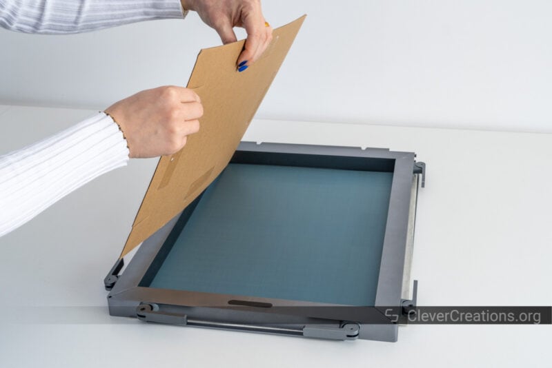 A person removing a piece of protective carton from a screen printing mesh.
