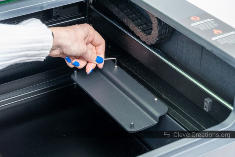 A hand using an Allen key to secure a bracket in a laser cutting machine.