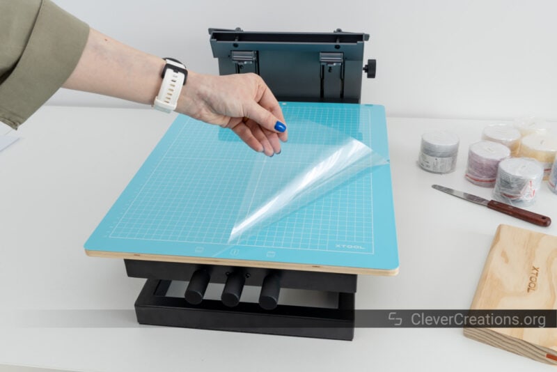 A person removing a piece of clear plastic from a blue cutting mat.