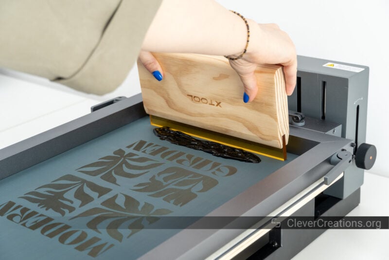 Someone using a squeegee to spread black paint on a design during screen printing.