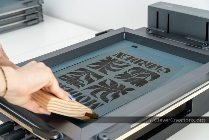 Someone using a squeegee to spread black paint on a design during screen printing.