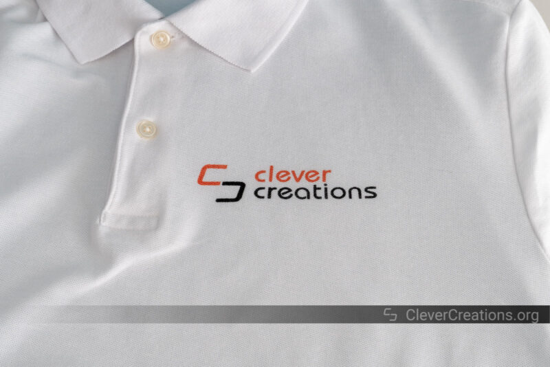 A white polo shirt with 'Clever Creations' logo screen printed on it.