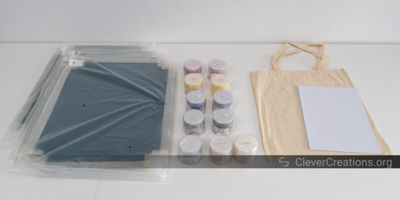 Several paints, mesh screens, a tote bag, and white carton laid out on a table.